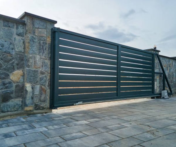Wide automatic sliding gate with remote control installed in high stone fense wall. Security and protection concept.
